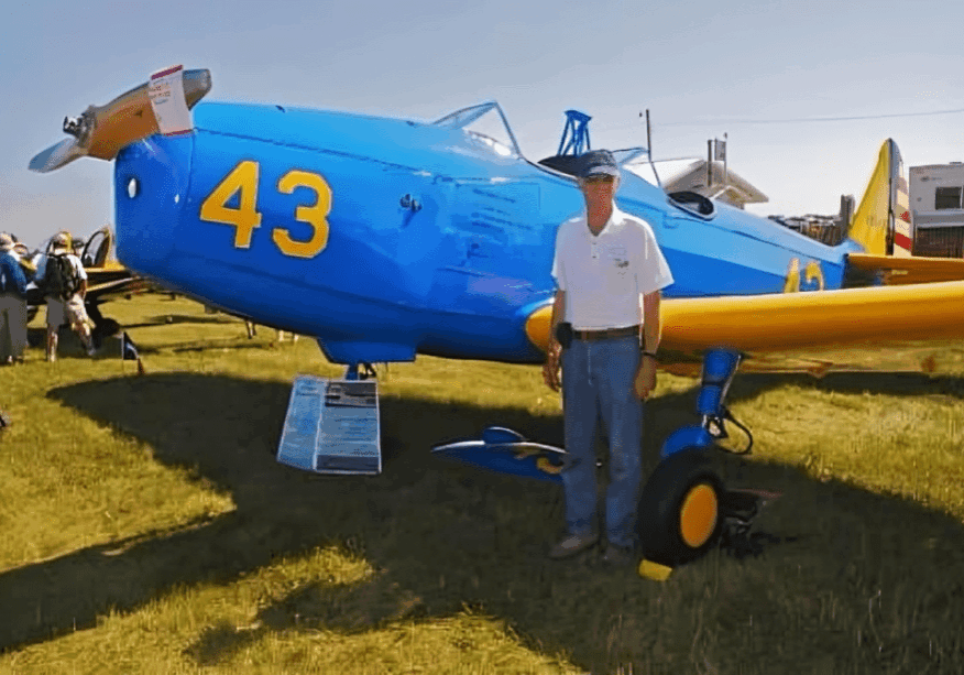 Man standing beside blue vintage airplane.